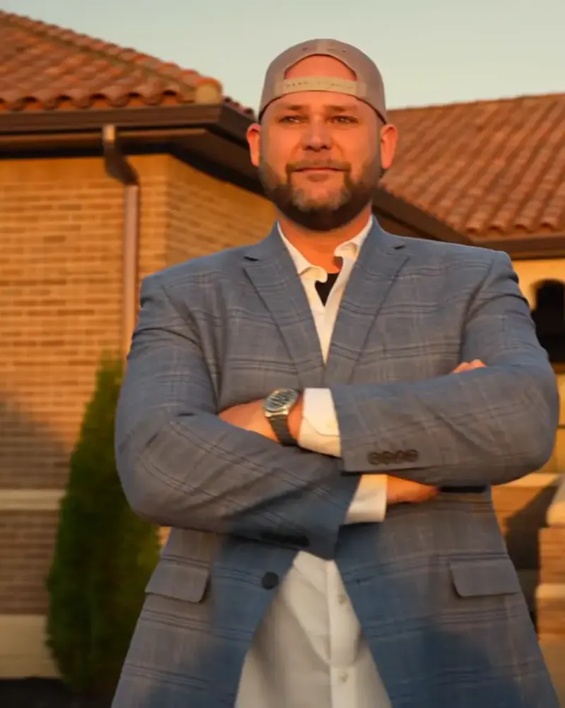 Justen Newton standing in front of a clay tile roof at sunset, arms crossed