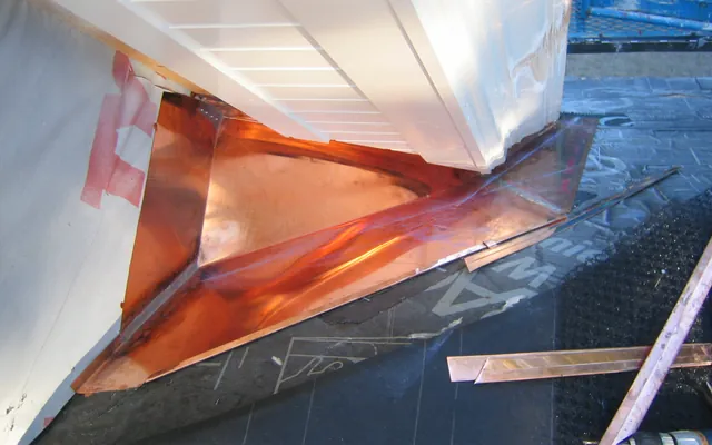 Example photo: Copper cricket, a small peaked saddle, set on the up-slope side of a chimney over underlayment